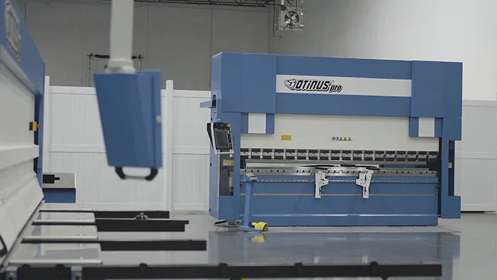 Otinus Pro press brake displayed in a clean industrial showroom, featuring a CNC-controlled bending area, front support arms, and a polished concrete floor.