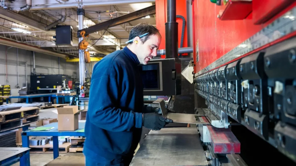 Operator positioning a metal sheet at a CNC press brake in an industrial production hall.