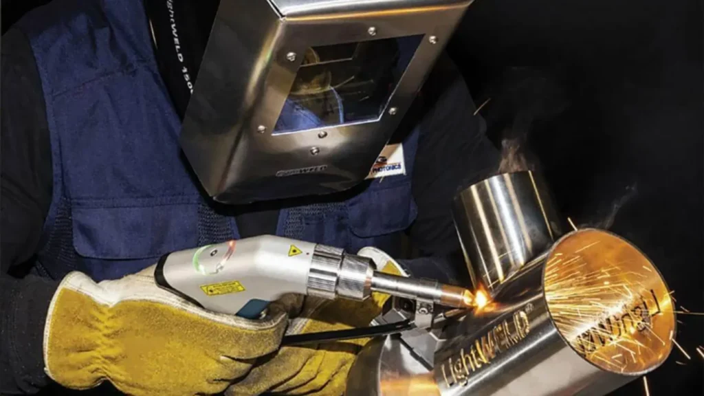 Operator w masce ochronnej wykonuje precyzyjne spawanie laserowe elementów ze stali nierdzewnej, generując jasne iskry podczas łączenia metalu.