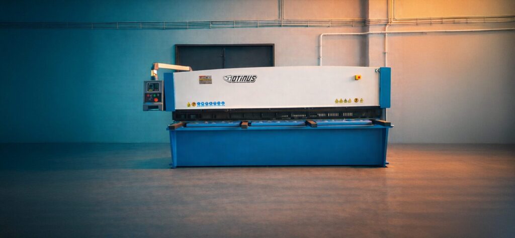 Frontowy widok nożyc gilotynowych Otinus Base w hali przemysłowej, eksponujący symetryczną, solidną konstrukcję, precyzyjny mechanizm cięcia oraz czytelny panel sterowania zaprojektowany z myślą o wydajnej pracy.