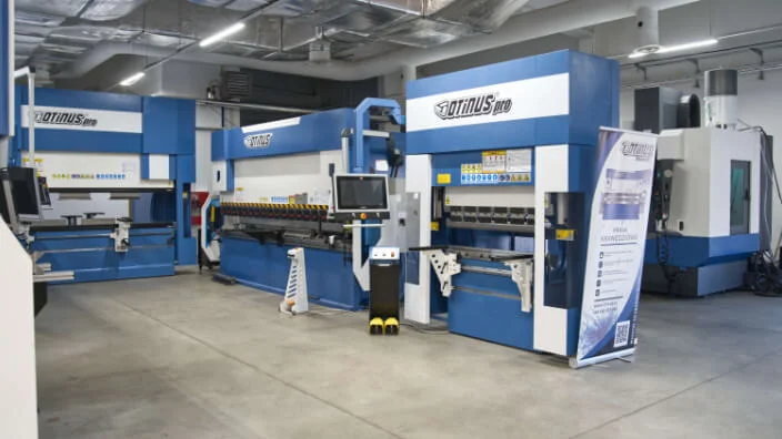 Otinus Pro press brakes displayed inside a modern industrial showroom, arranged in a clean production hall with operator panels, safety foot pedals, and branded informational banners.