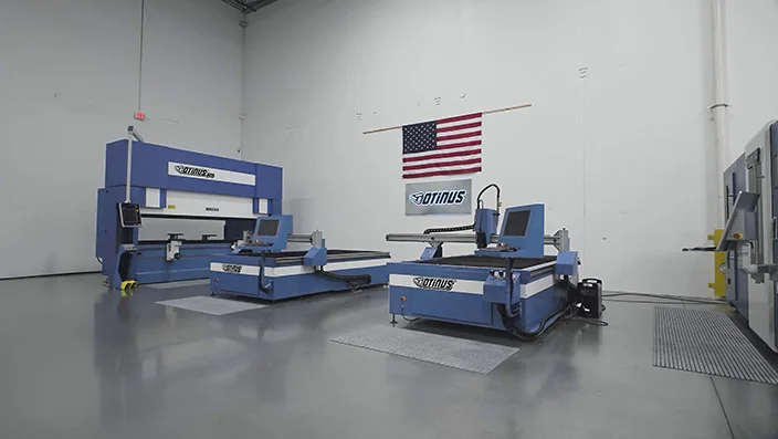 Modern industrial showroom featuring Otinus CNC machines arranged on a polished floor, with an American flag displayed on the wall, highlighting a professional manufacturing environment.